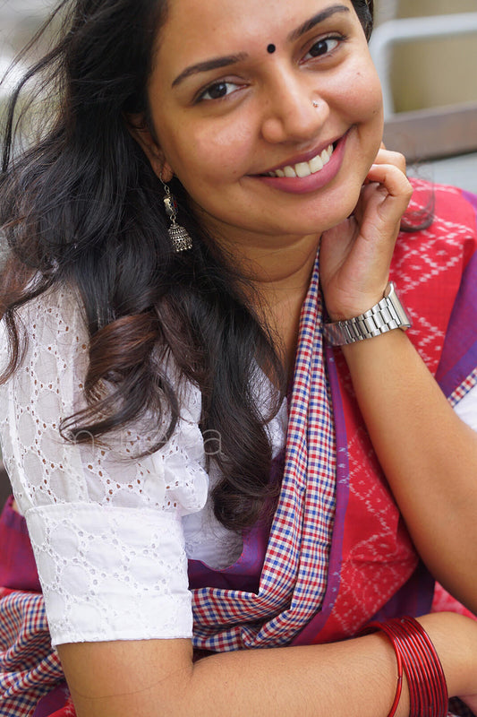 Woman wearing a red and purple saree with a white blouse, smiling.